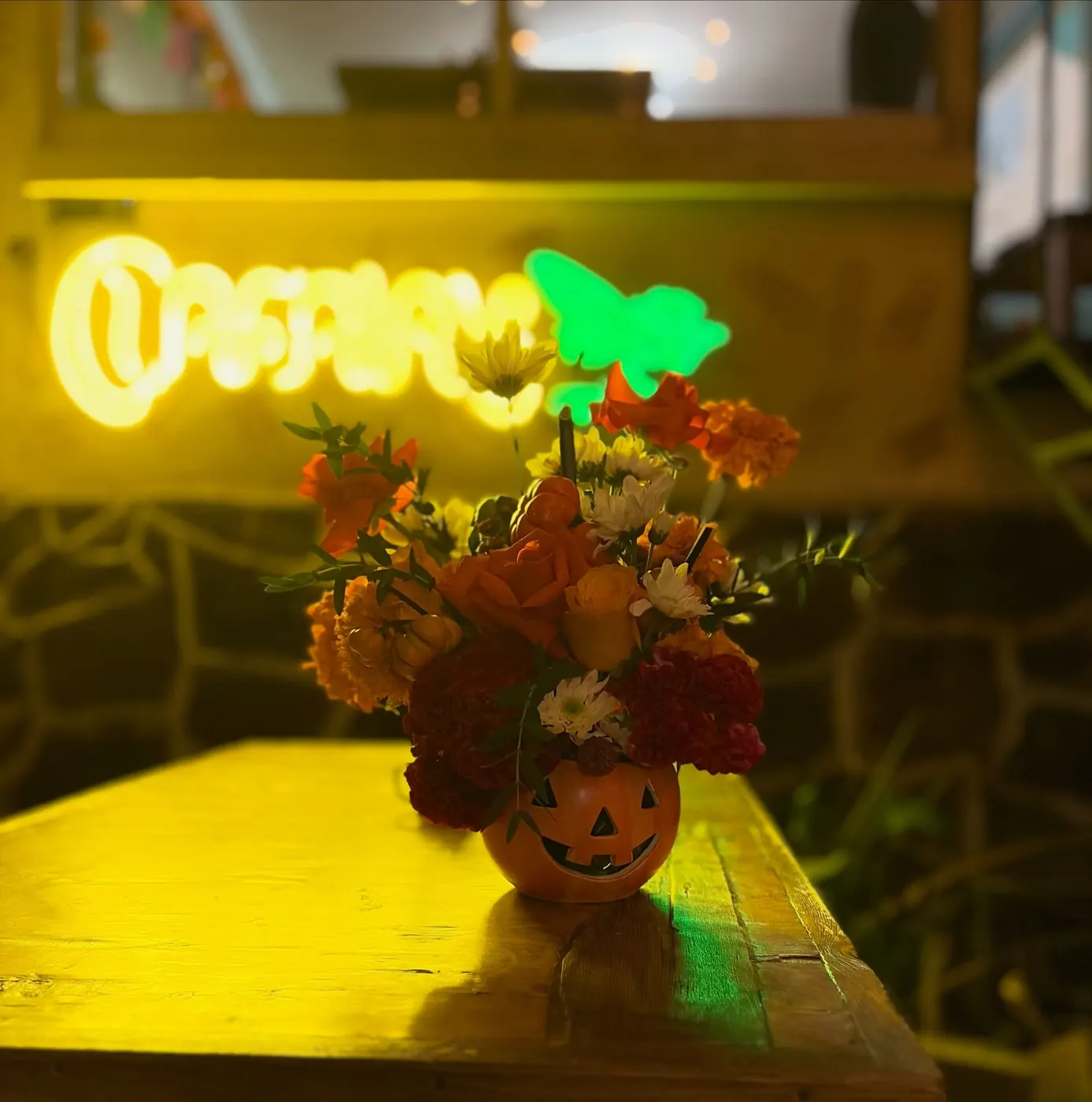 Letrero de neón amarillo de Cafairy sobre un arreglo de flores en calabaza